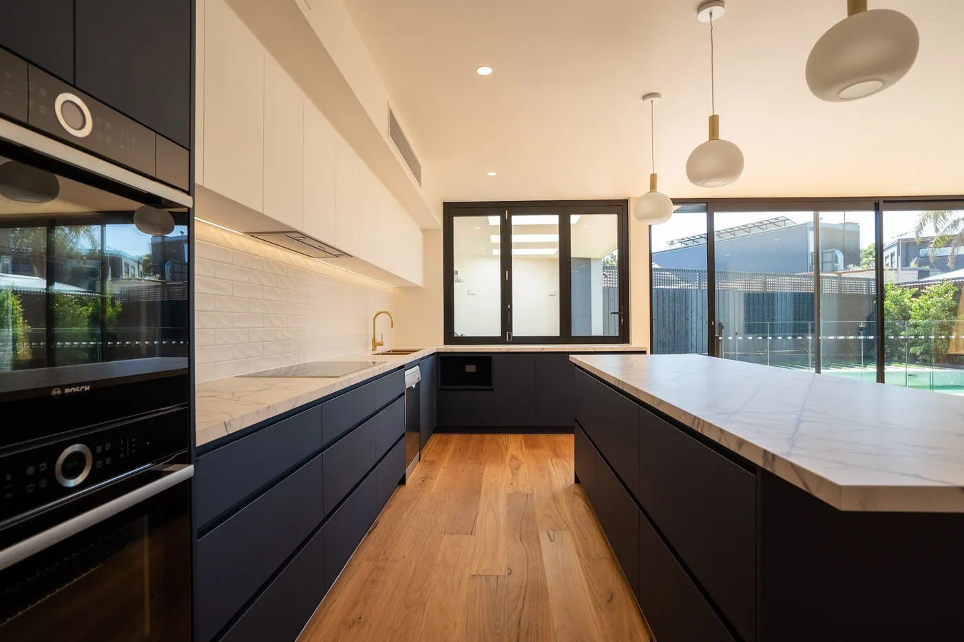 Navy kitchen with marble splashback and pool view — Nicon Built